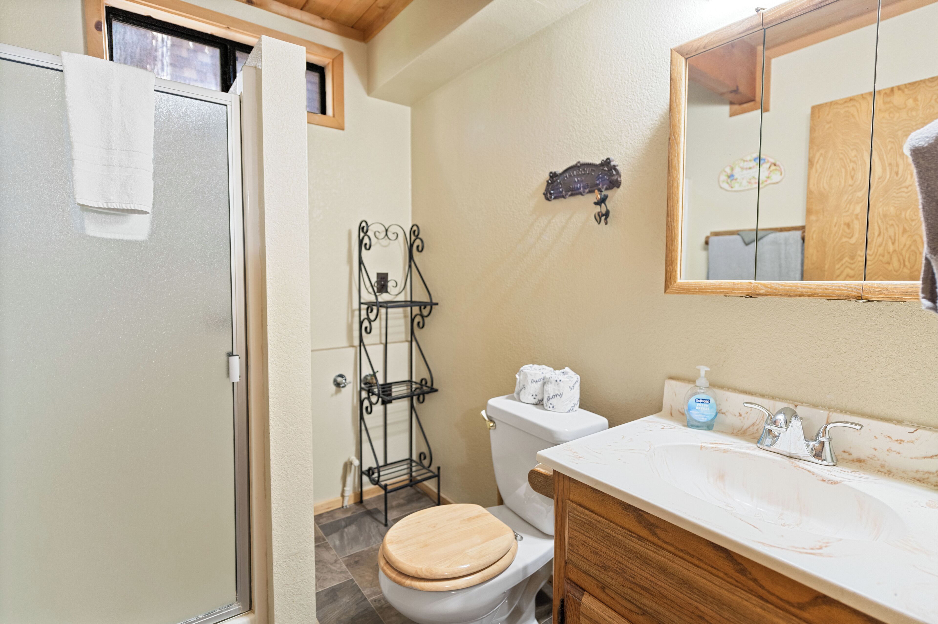 A bathroom with a wooden toilet, a white sink with a mirror above it, and a towel hanging on the door.