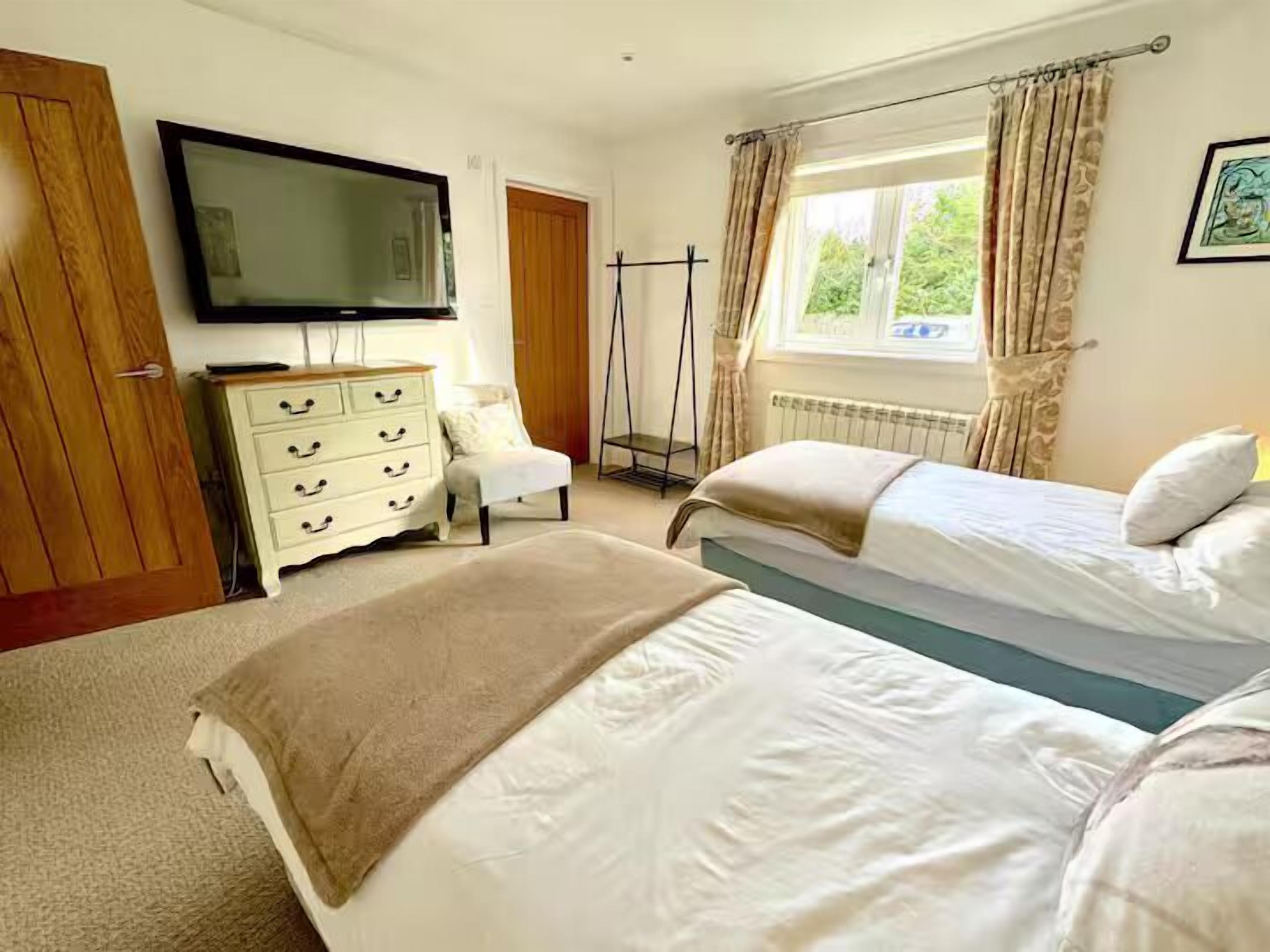 A bedroom with two beds, a TV, a dresser, and a window with curtains.