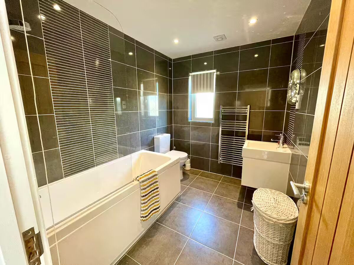 A modern bathroom with dark tiles, a white bathtub, a toilet, and a sink.