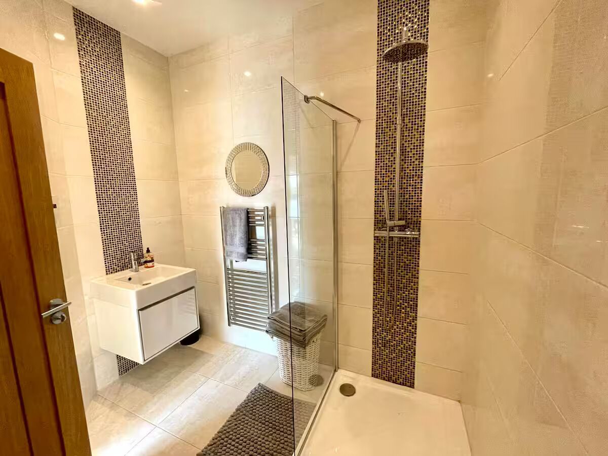 Een moderne badkamer met een douchecabine van glas, een wit wastafelmeubel en een betegelde douche.