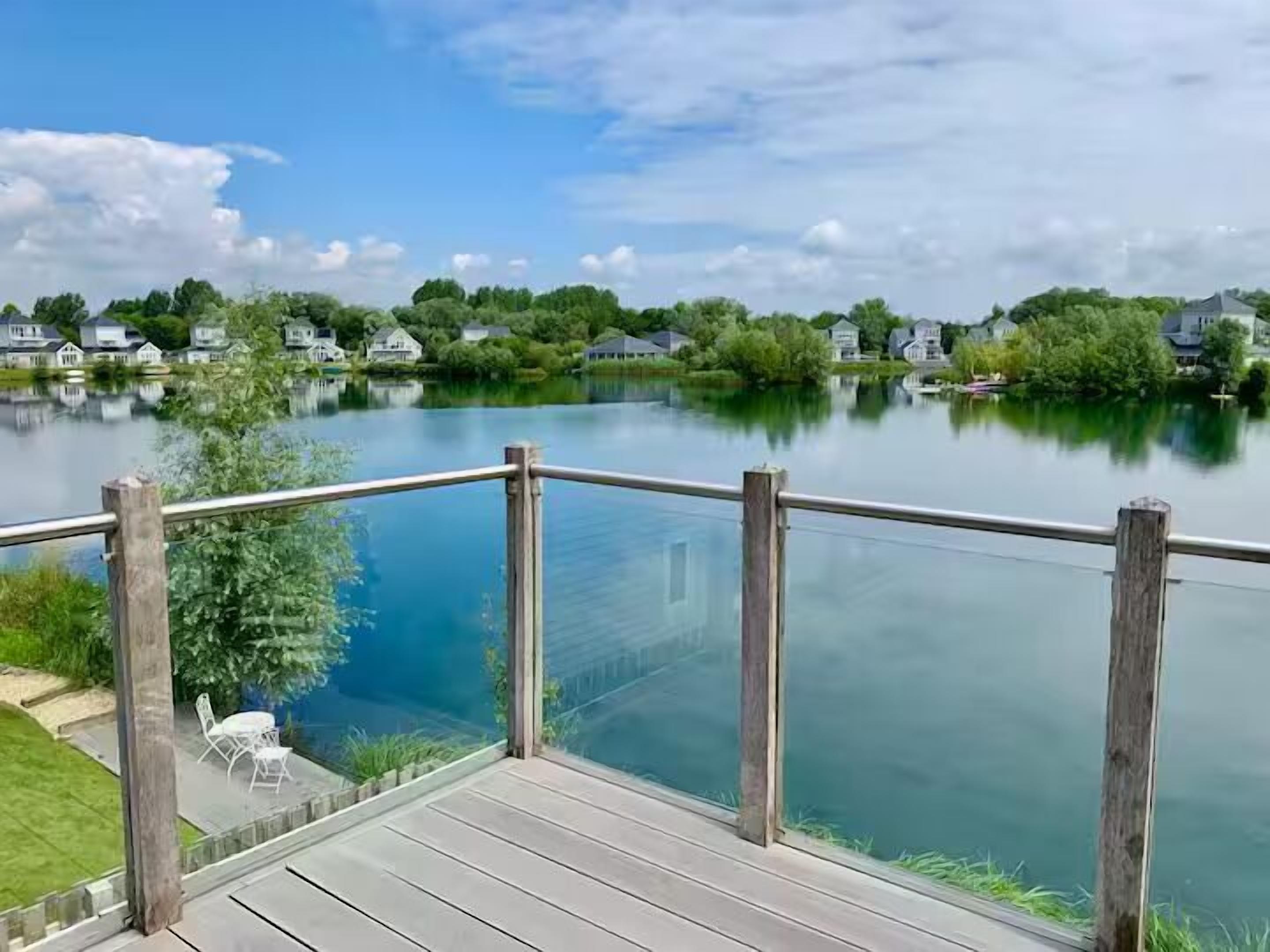 A wooden deck overlooking a calm lake with houses in the background.