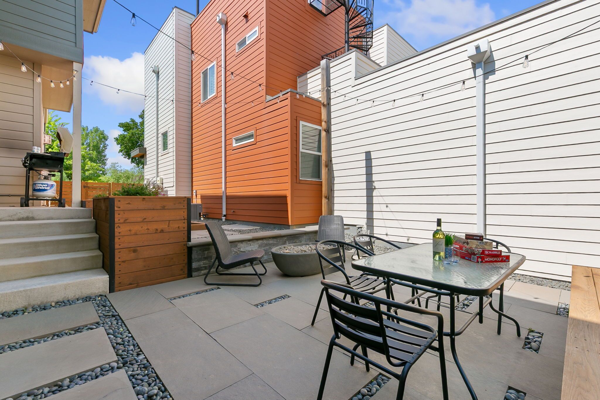 A patio with a table and chairs, a barbecue grill, and a wooden fence.