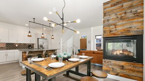 Een moderne keuken met een houten eettafel, hanglampen en een inbouwvuurplaats.