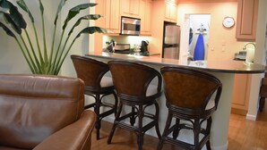 A modern kitchen with wooden cabinets, a stainless steel refrigerator, and a built-in microwave. There are three bar stools and a large potted plant. - Wild Oak Bay - 3/2 Beaches 15 minute drive (Bradenton)
