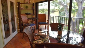 A sunlit patio with wicker furniture, a glass table, and a view of trees and a fence. - Wild Oak Bay - 3/2 Beaches 15 minute drive (Bradenton)