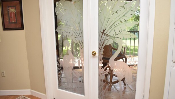 A door with frosted glass panels featuring a leaf and bird design, leading to an outdoor patio area with a table and chairs. - Wild Oak Bay - 3/2 Beaches 15 minute drive (Bradenton)
