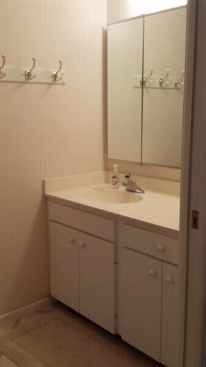 Une petite salle de bain blanche, avec un seul lavabo, un miroir et un meuble de rangement.