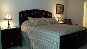Un lit bien fait, recouvert d’une couvre-lit à rayures et agrémenté de deux oreillers, avec deux tables de chevet de chaque côté, sur lesquelles sont posées des lampes.