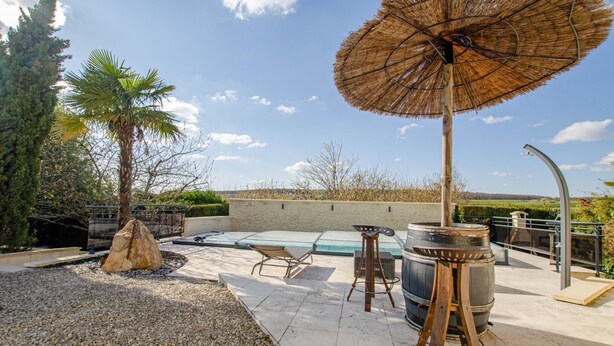 A rooftop pool area with a hot tub, lounge chairs, and a pergola with a thatched umbrella.