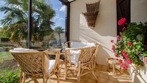 A sunlit patio with wicker furniture and a view of palm trees.