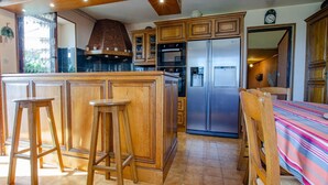 A kitchen with wooden cabinets, a stainless steel refrigerator, and a bar stool.