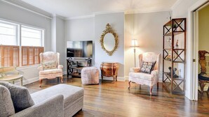 A spacious living room with a large television, two armchairs, a sofa, and a wooden floor.