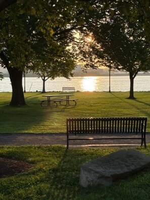 Un parc avec un banc et une table de pique-nique, un banc en pierre et une étendue d’eau en arrière-plan.