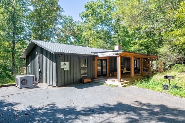 A cabin with a metal roof, a porch, and a small attached building.
