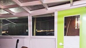 A room with a green door, a wooden guitar, two chairs, and a small round table. - Designer House (수원)