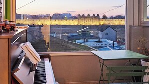 A piano in a room with a large window overlooking a cityscape. - Designer House (수원)