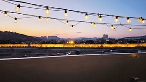 A rooftop with string lights and a cityscape in the background. - Designer House (수원)