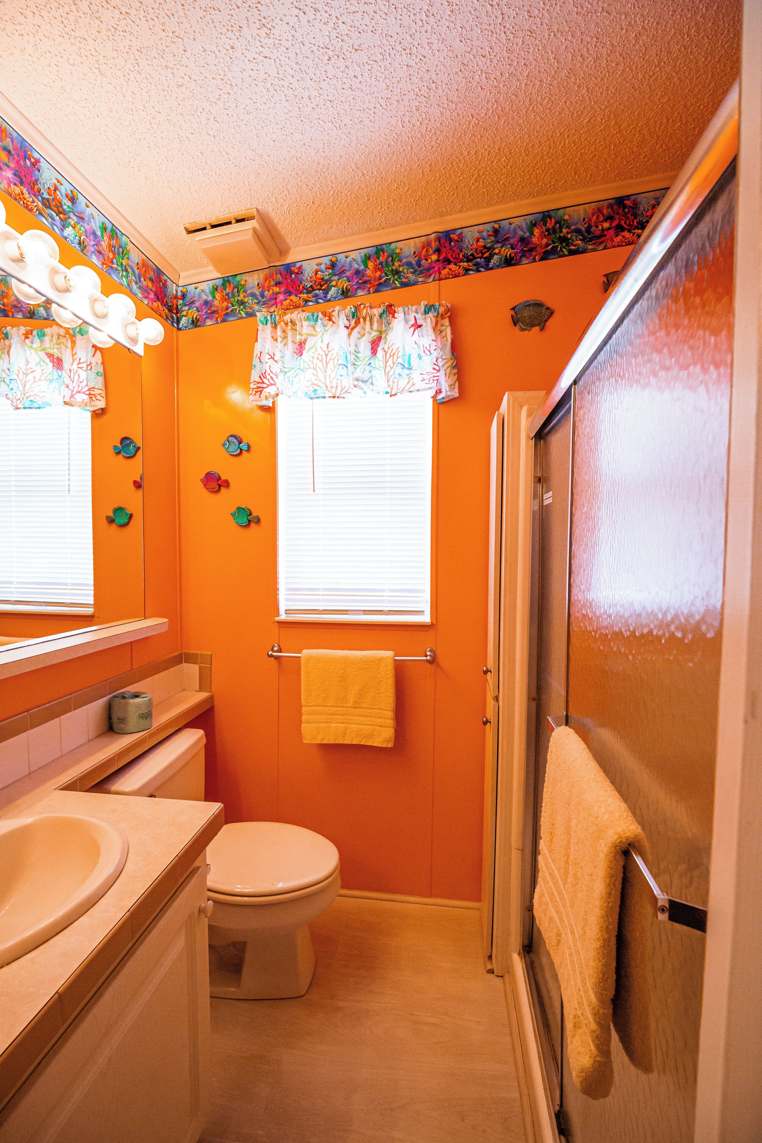 Un baño con pared naranja, un inodoro, un lavamanos y una ducha.