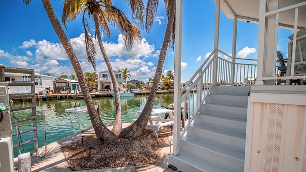 A waterfront property with a white staircase leading to a covered deck, palm trees, and a marina with boats. - Sea Cow Key Cottage - Venture Out Unit 585 (Cudjoe Key)