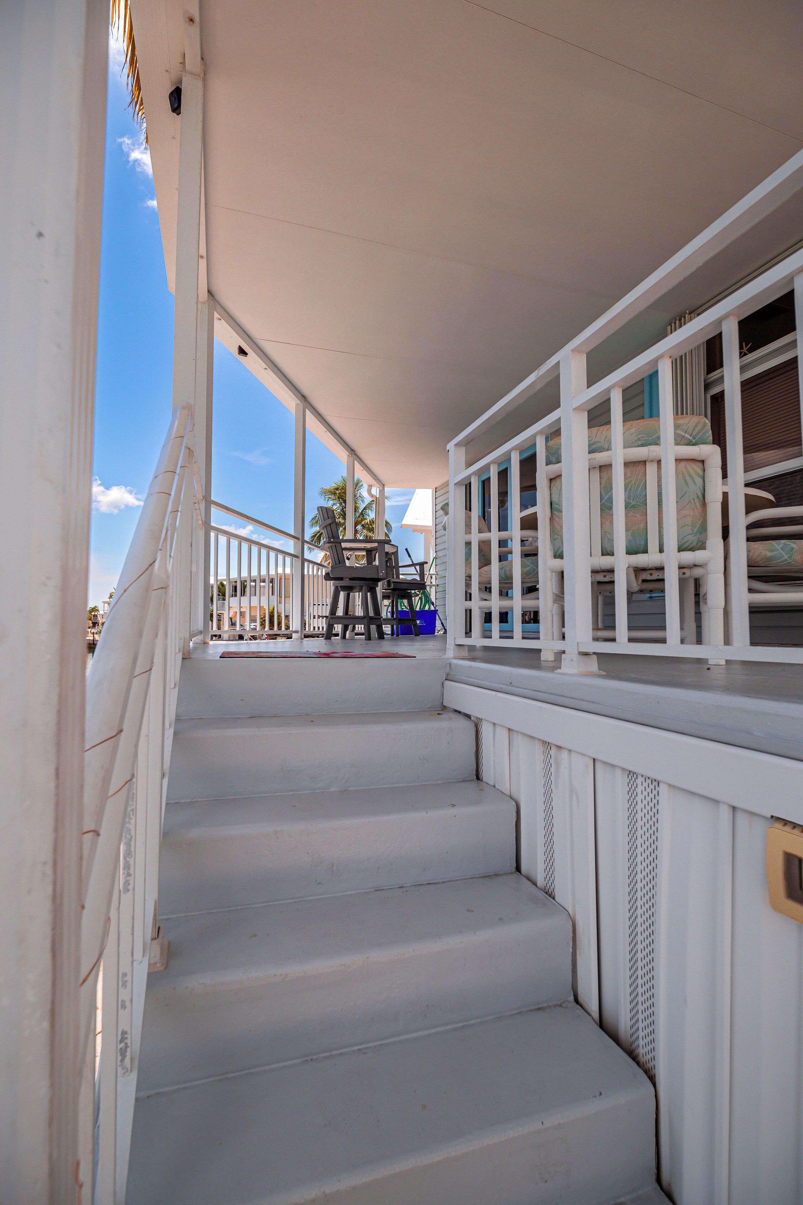 A staircase leading to a balcony with a railing, a view of the sky, and a chair on the balcony.