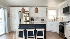 A modern kitchen with white cabinets, a central island with stools, a large island stove, and hanging pendant lights. - Sea Cow Key Cottage - Venture Out Unit 585 (Cudjoe Key)