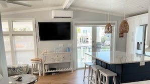 A modern kitchen with a large island, white cabinetry, and a flat-screen TV mounted above the counter. - Sea Cow Key Cottage - Venture Out Unit 585 (Cudjoe Key)