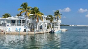 A waterfront property with multiple white buildings, palm trees, and a dock with a boat. - Sea Cow Key Cottage - Venture Out Unit 585 (Cudjoe Key)