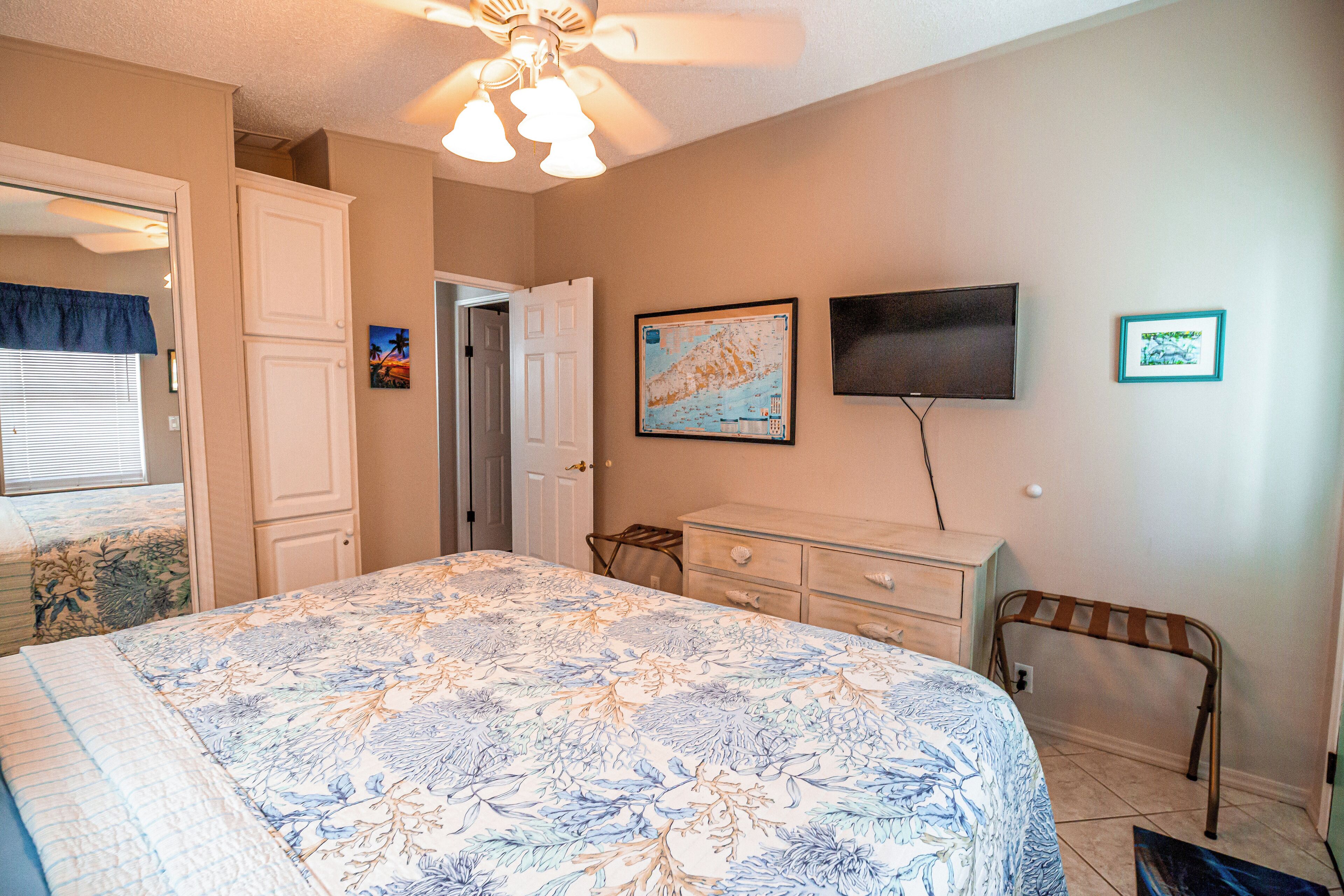 A bedroom with a bed, a dresser, a television, and a map on the wall.