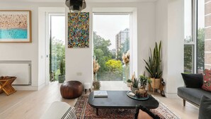 A modern living room with a large window, a black coffee table, a sofa, and various plants. - Sun-Drenched Shoreditch 2BR Penthouse with Balcony (London)