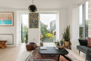 A modern living room with a large window, a black coffee table, a sofa, and various plants.
