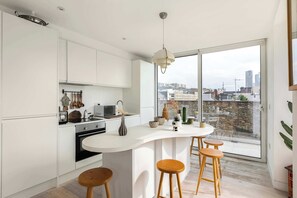 Una cocina moderna con una isla grande, taburetes de bar y vistas a la ciudad a través de amplios ventanales.