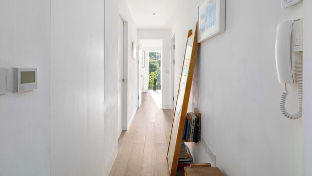 A hallway with a wooden floor, white walls, a telephone, and a framed picture. - Sun-Drenched Shoreditch 2BR Penthouse with Balcony (London)