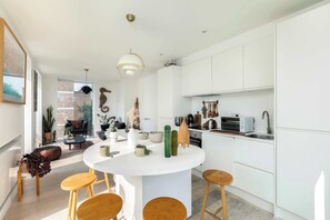 A modern kitchen with white cabinetry, a round island with stools, and a dining area with a sofa and coffee table.