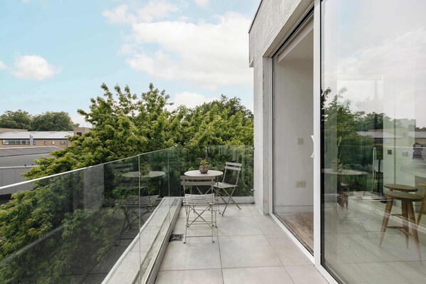 A balcony with a glass railing, a table, and two chairs.