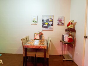 A dining area with a table set for two, a vase with flowers, and wall art. - Amigas Transient House (Santo Tomas)