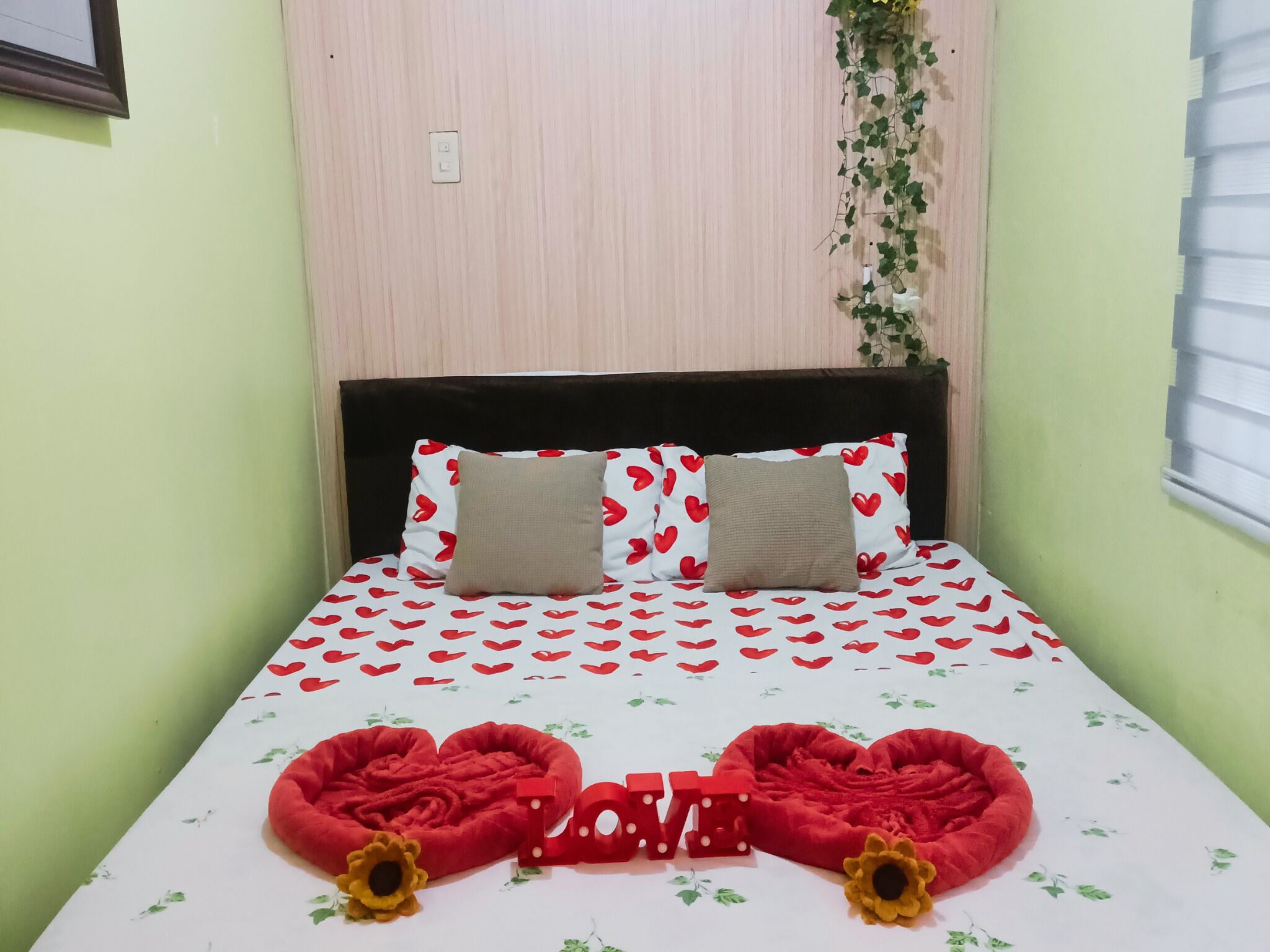 A bed with a heart-patterned bedspread, two pillows, and a 'LOVE' decoration on the bed.