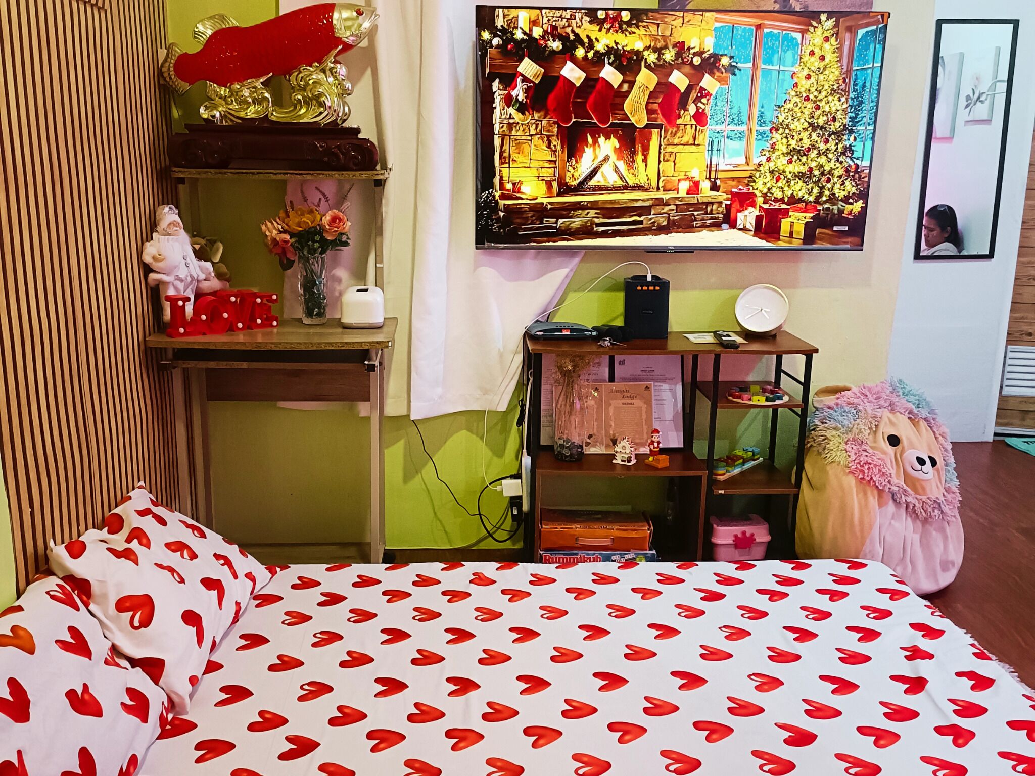 A cozy room with a bed, a shelf with various items, a fireplace, and a Christmas tree.