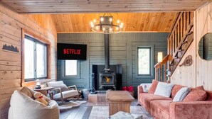 A cozy log cabin interior with a fireplace, a sofa, a chair, and a Netflix sign. - Woodsy Chalet Near Tremblant (Amherst)