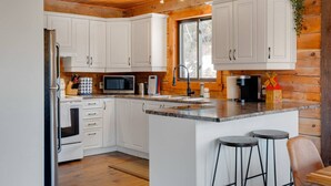 A modern kitchen with white cabinets, a granite countertop, a built-in microwave, and a window. - Woodsy Chalet Near Tremblant (Amherst)