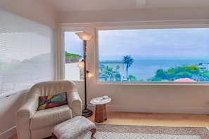Quarto com vista para o mar, uma cadeira, uma pequena mesa e um abajur.