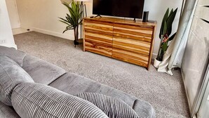 Een moderne woonkamer met een grijze bank, een houten kast, een flatscreen televisie en een potplant.