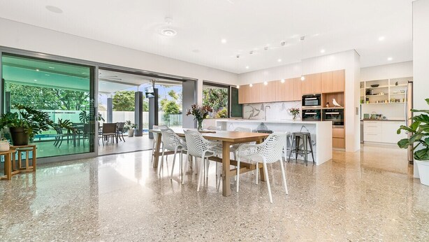 A modern kitchen with a central island, a dining area with white chairs, and a large glass door leading to an outdoor area. - Fred's at Fannie Bay (Fannie Bay)