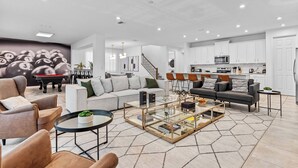 A spacious living room with a billiards-themed mural, a billiards table, and a kitchen area with white cabinets and modern appliances. - 9BR house sleeps 21 with spa and pool table (Kissimmee)