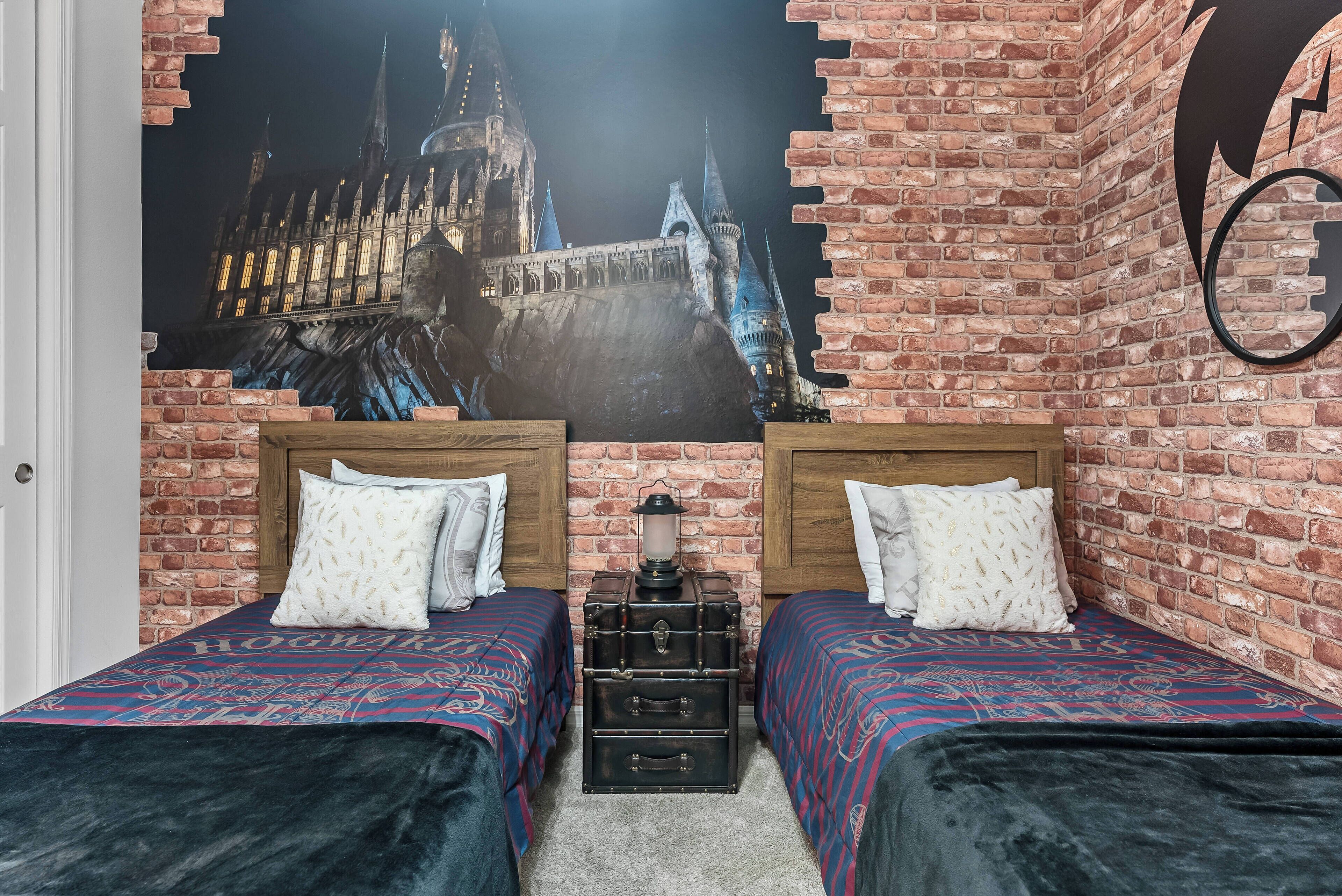 Una habitación con dos camas, una pared de ladrillo y un gran mural con temática de Hogwarts.