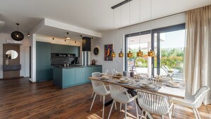 Une cuisine moderne avec des meubles de couleur turquoise, un îlot central et un coin repas comprenant une table en bois et des chaises blanches.