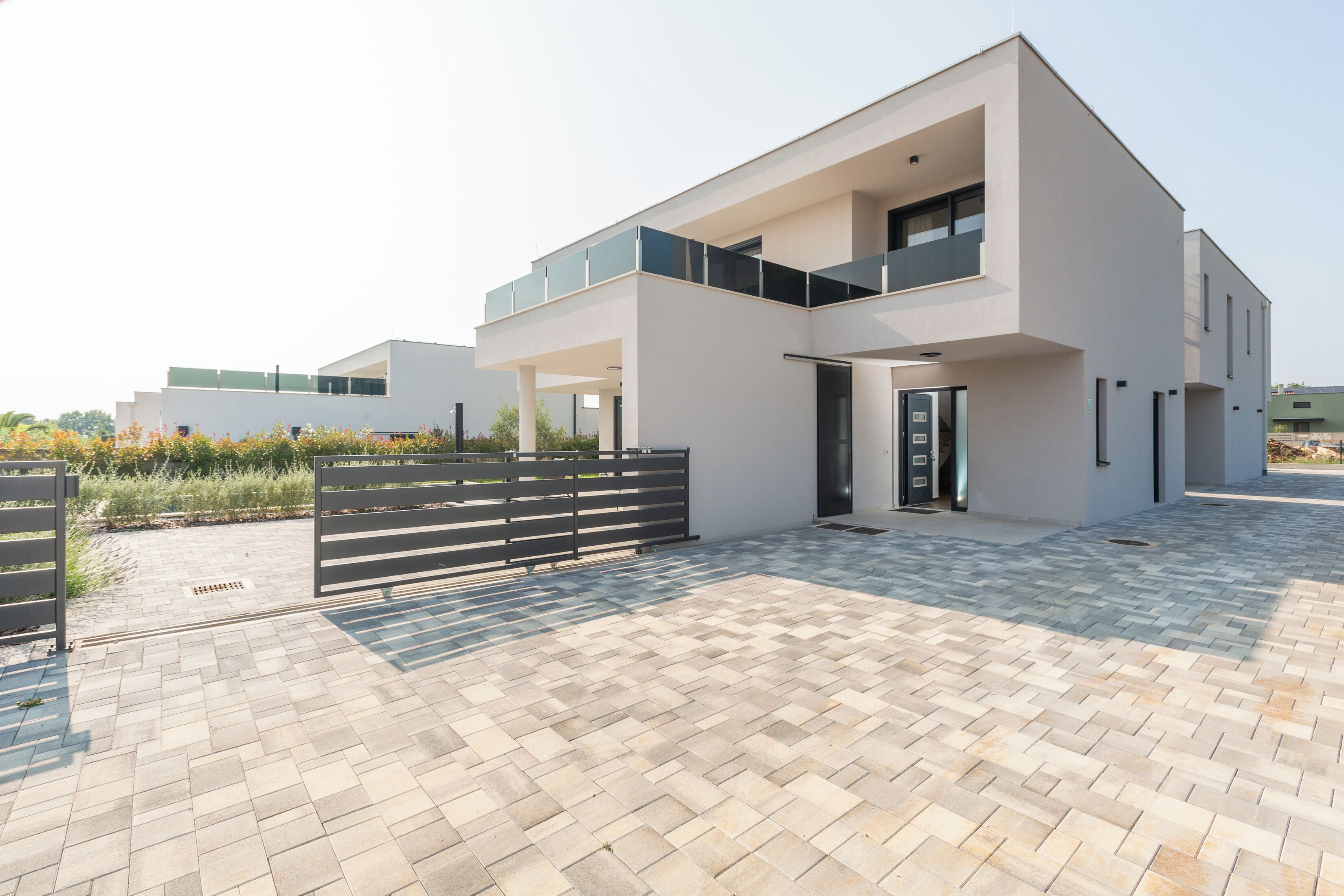 A modern two-story building with a flat roof, large windows, and a paved courtyard.