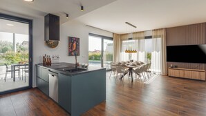 Une cuisine moderne avec un îlot central, un coin repas doté d’une grande table et un téléviseur posé sur un meuble en bois.