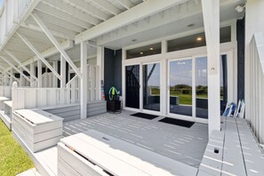 A covered outdoor area with a wooden deck, a black trash bin, and a set of outdoor furniture. - Sandpiper Sunrise - Hosted by Moore AI Rentals (Fernandina Beach)