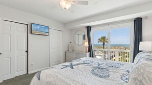 A bedroom with a bed, a ceiling fan, a window with a view of the beach, and a door. - Sandpiper Sunrise - Hosted by Moore AI Rentals (Fernandina Beach)