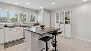 A modern kitchen with white cabinetry, a marble island, and bar stools. - Sandpiper Sunrise - Hosted by Moore AI Rentals (Fernandina Beach)